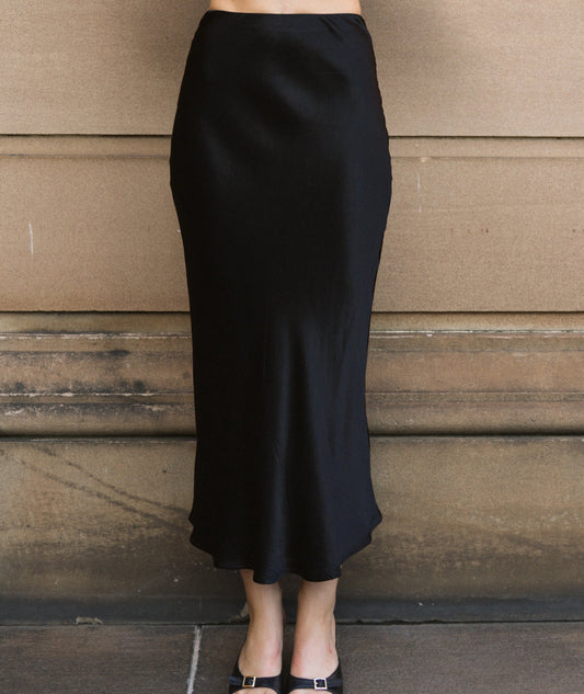 Person wearing a black skirt standing against a wooden wall.