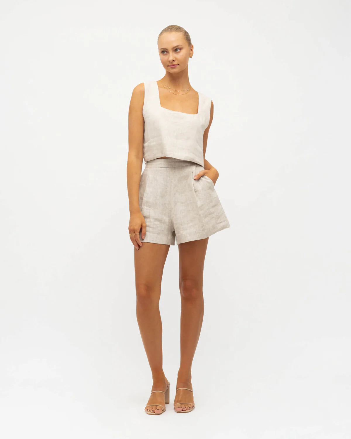 Woman wearing a white sleeveless top and beige shorts on a white background